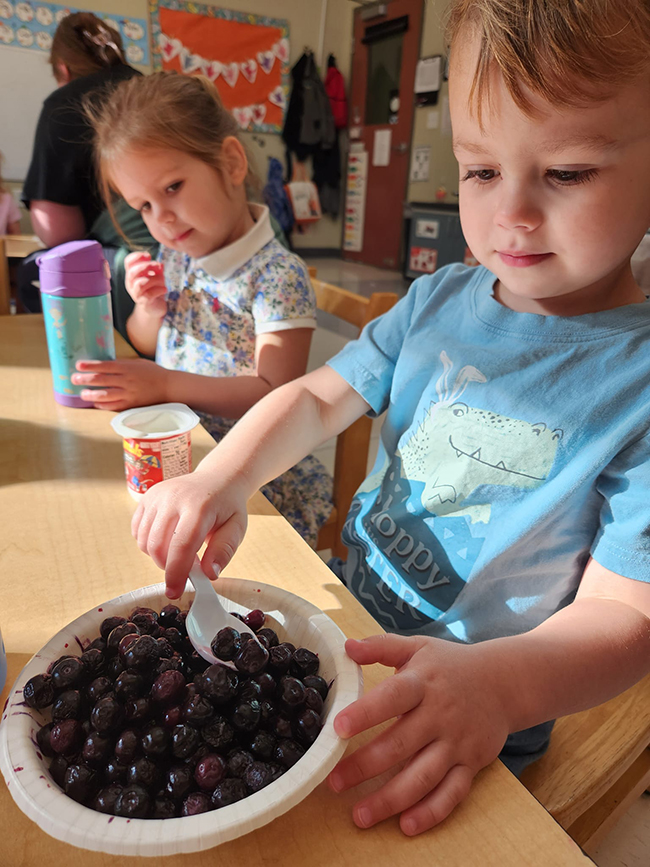 Little boy spooning blueberries as a little girl watches